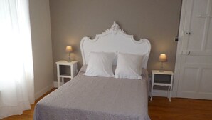 Una cama bien hecha con cabecera blanca y dos mesitas de noche, cada una con una lámpara.