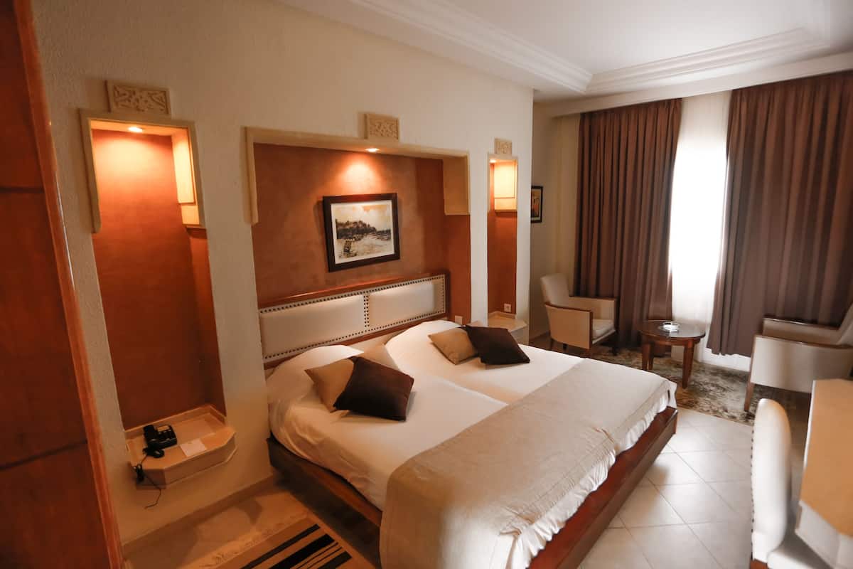 Une chambre d’hôtel avec un grand lit, deux tables de chevet, une chaise, un bureau et une vue sur l’extérieur.