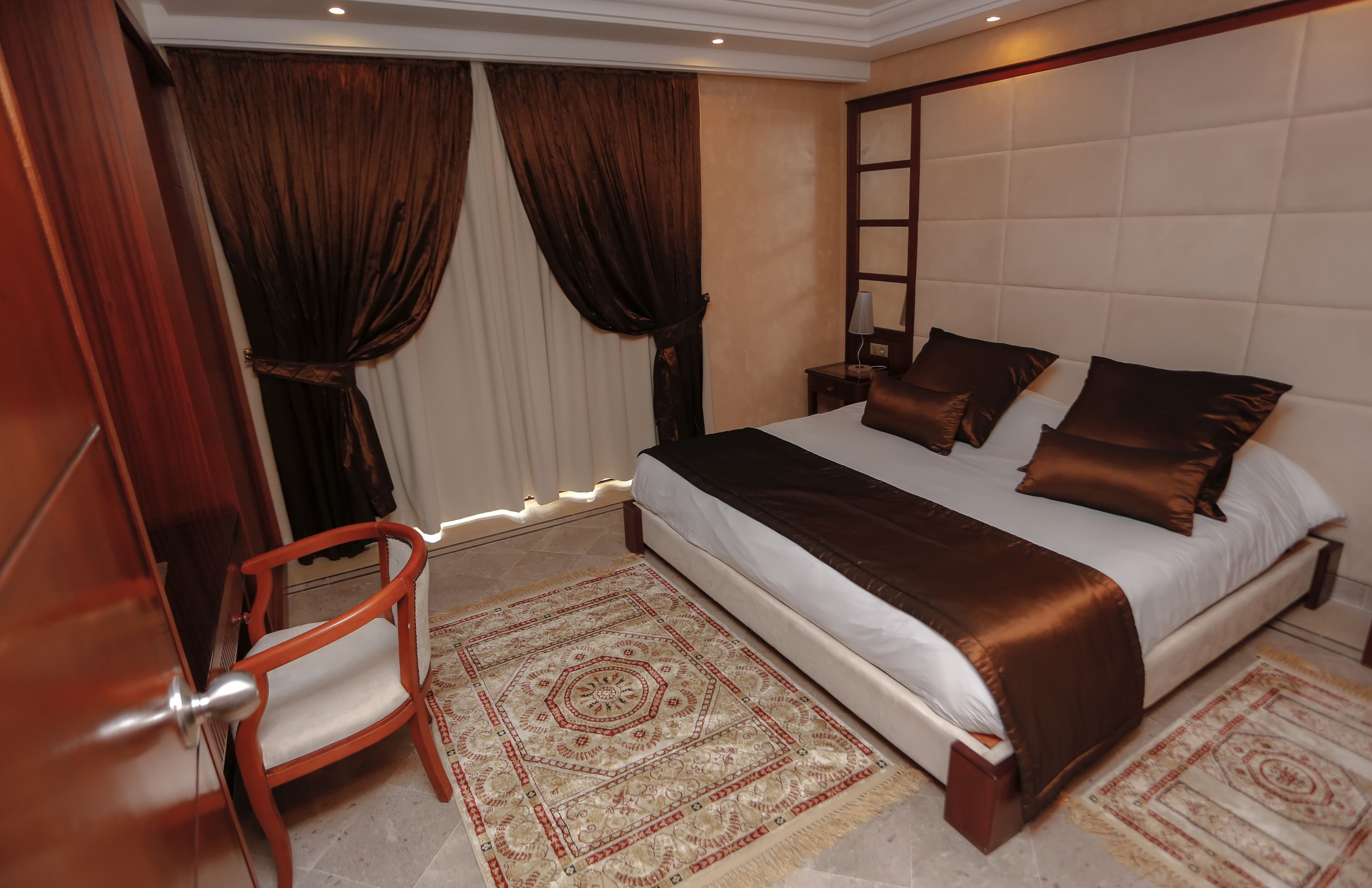 A neatly arranged bedroom with a large bed, a wooden chair, and a patterned rug.