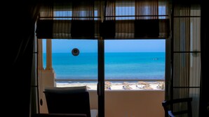Ein Balkon mit Meer- und Strandblick, ein Tisch mit Getränken und ein Stuhl.
