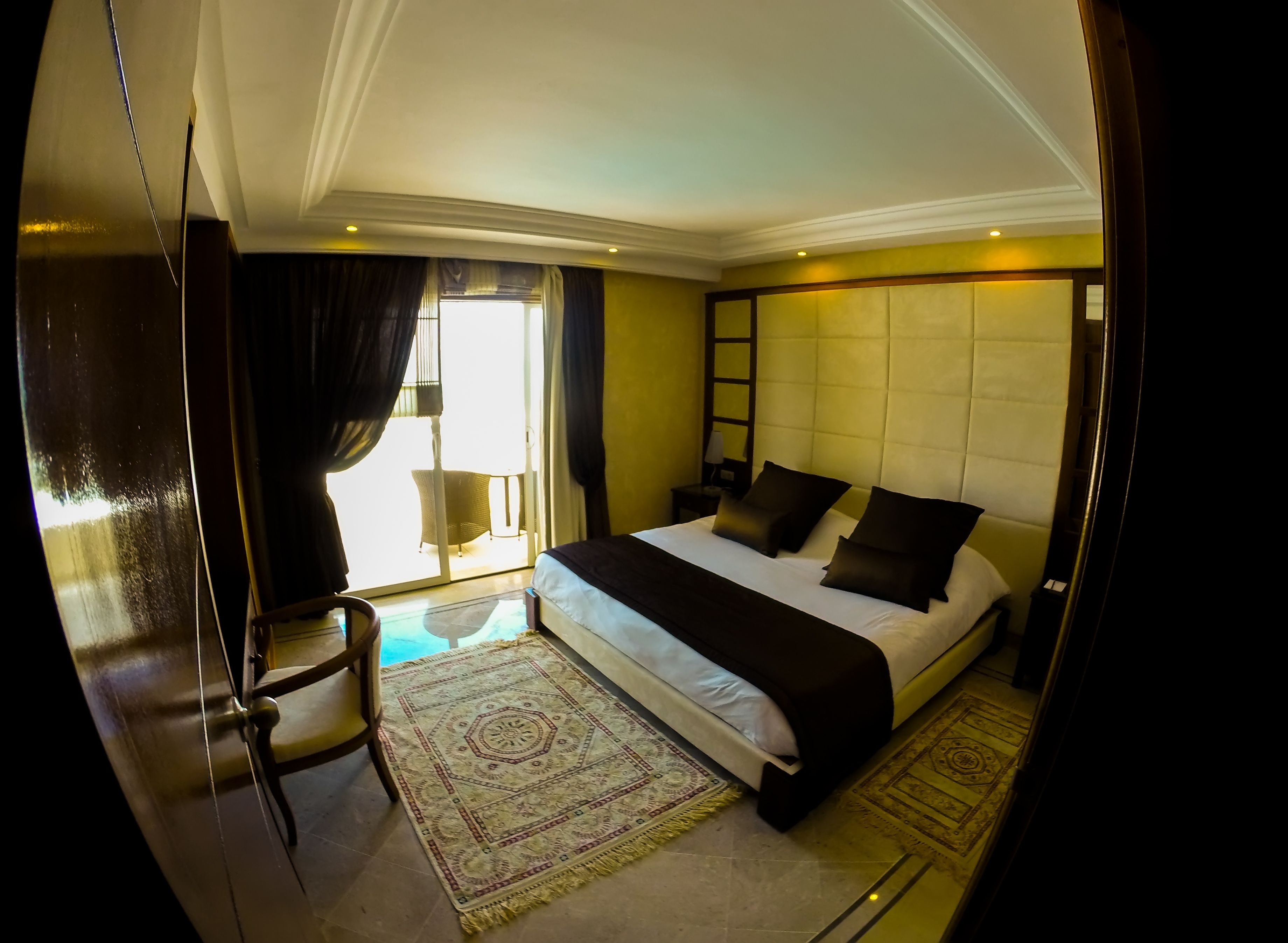 A hotel room with a large bed, a chair, a small table, and a view of the outdoors.