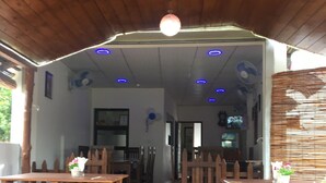 Interior de restaurante con mesas y sillas de madera, una alfombra roja y un techo con luces azules.