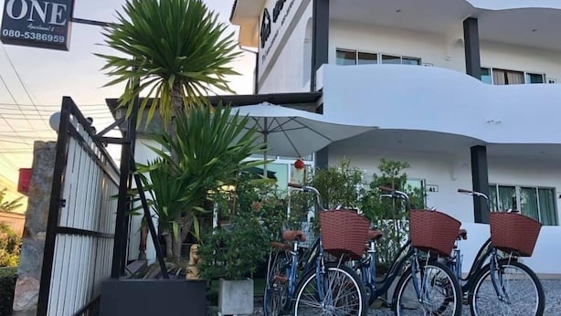 Un edificio moderno con un letrero que dice "The ONE" y un número de contacto. Hay bicicletas con cestas estacionadas adelante.
