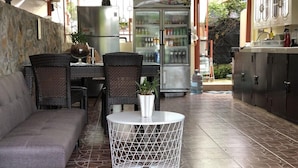 Un patio exterior con sofá, sillas de mimbre, una mesa redonda y un refrigerador.