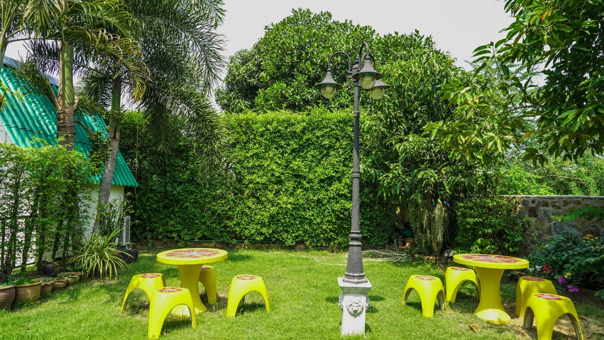 Un jardín con un pabellón, mesas amarillas y un farol decorativo.
