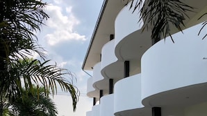 Un edificio moderno con paredes exteriores blancas y balcones. Hay plantas en macetas y un sendero de grava que conduce a la entrada.