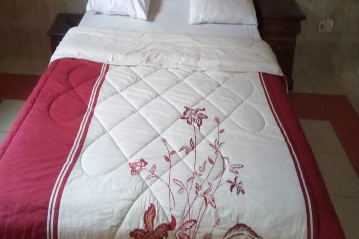 A bed with a white quilt and red accents, a wooden headboard, and two bedside tables.