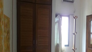 A room with a wooden wardrobe, a window with curtains, and a standing heater. - Complexe Hôtelier Paris Village (Abidjan)