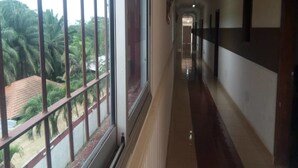 A long, narrow hallway with a window on the left side, allowing a view of palm trees and a building outside. - Complexe Hôtelier Paris Village (Abidjan)