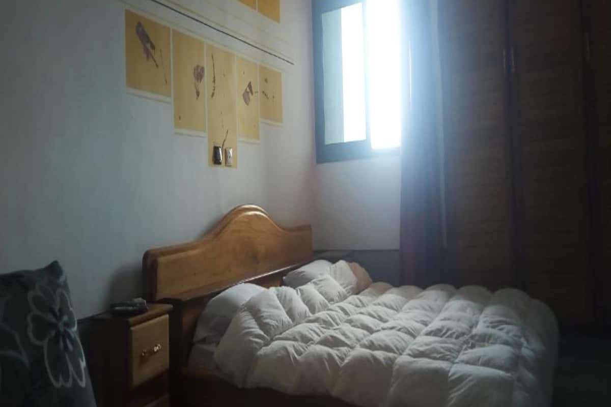 A bedroom with a wooden bed, a nightstand, a dresser, and a window with natural light.