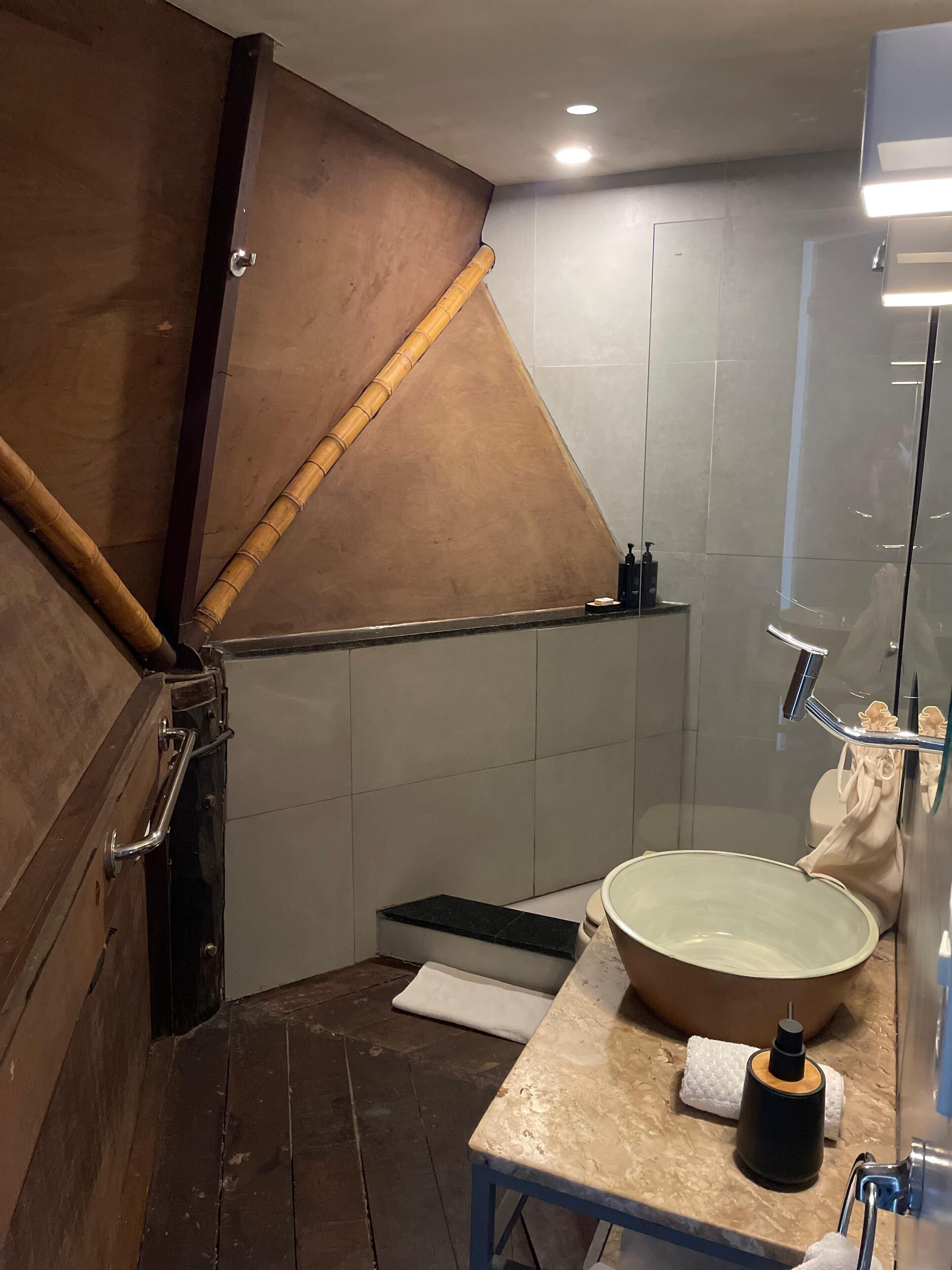 Une salle de bain avec un plafond en pente en bois, un grand lavabo avec un receveur et une douche à l’italienne en verre.