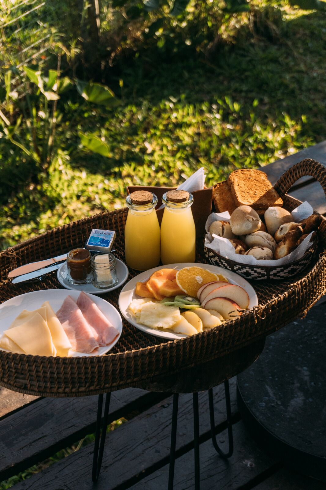 Piknik-varustelu, johon kuuluu rottinkikori, jossa on leipää, hedelmiä ja pullo mehua.