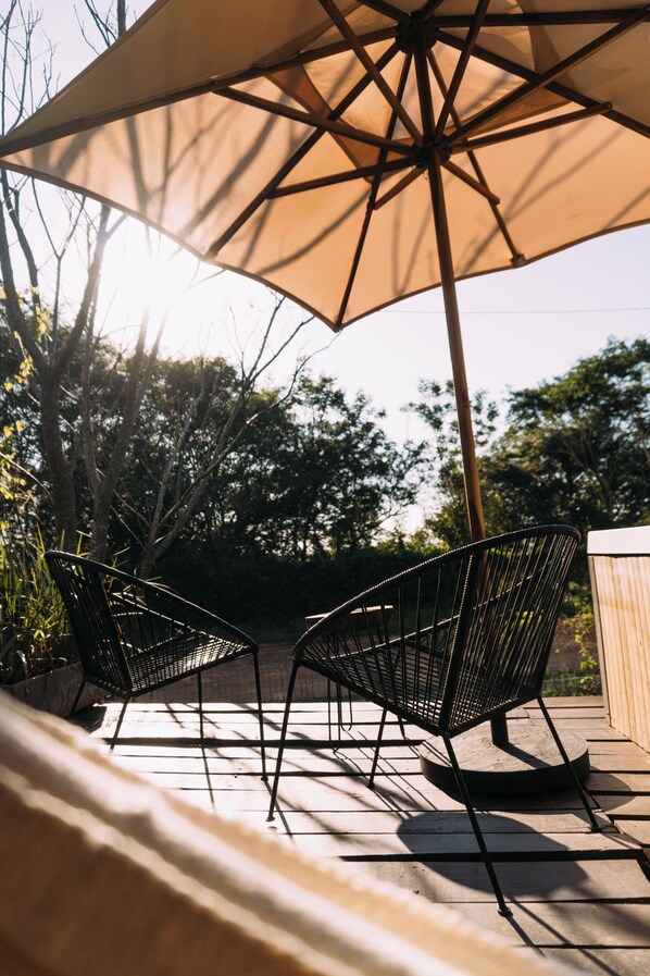 An outdoor patio with two black metal chairs and a beige umbrella providing shade. - Tava Glamping Lago (San Bernardino)