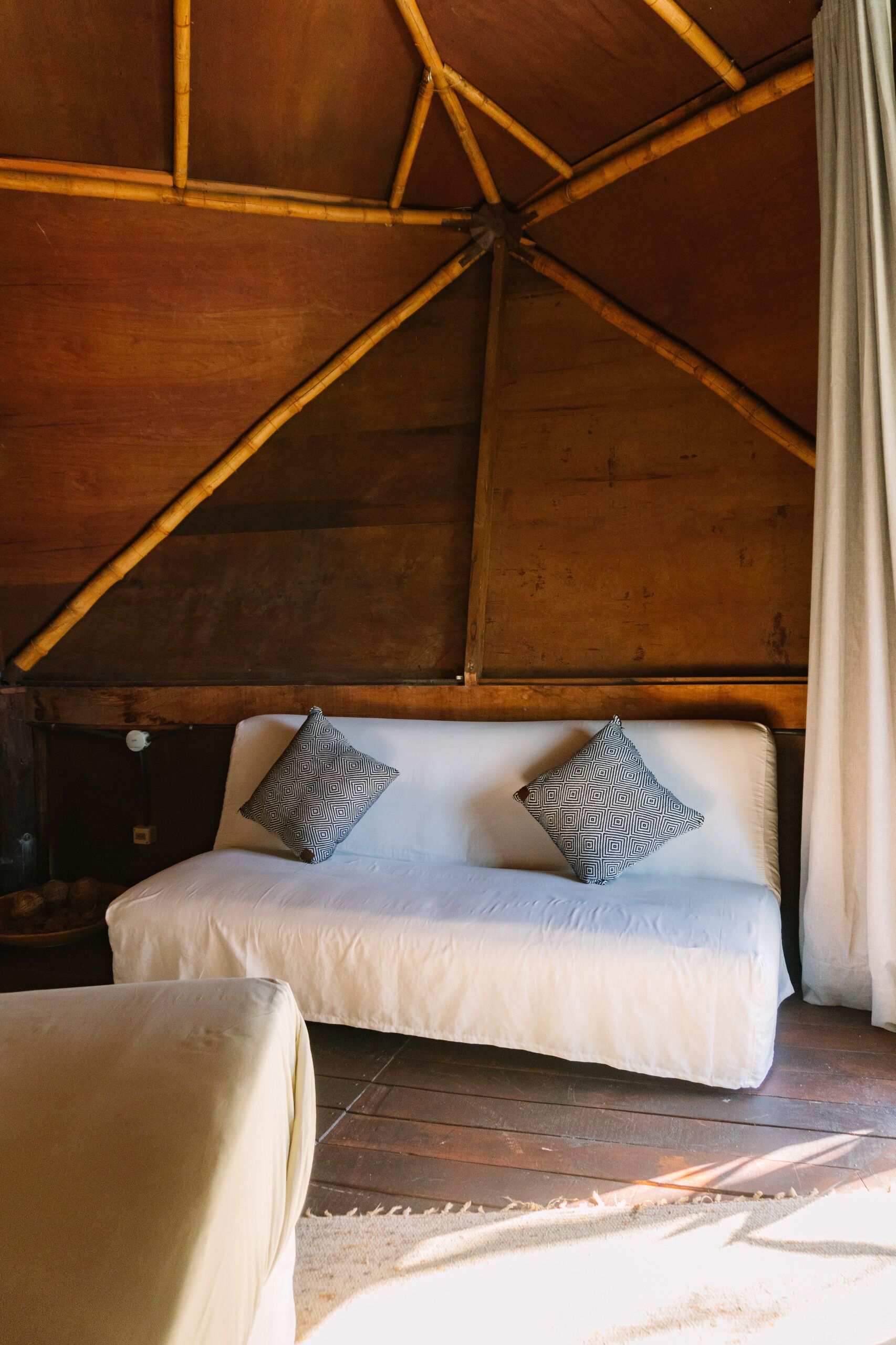 Una habitación acogedora con techo de madera, un sofá blanco con almohadones estampados y una mesita.