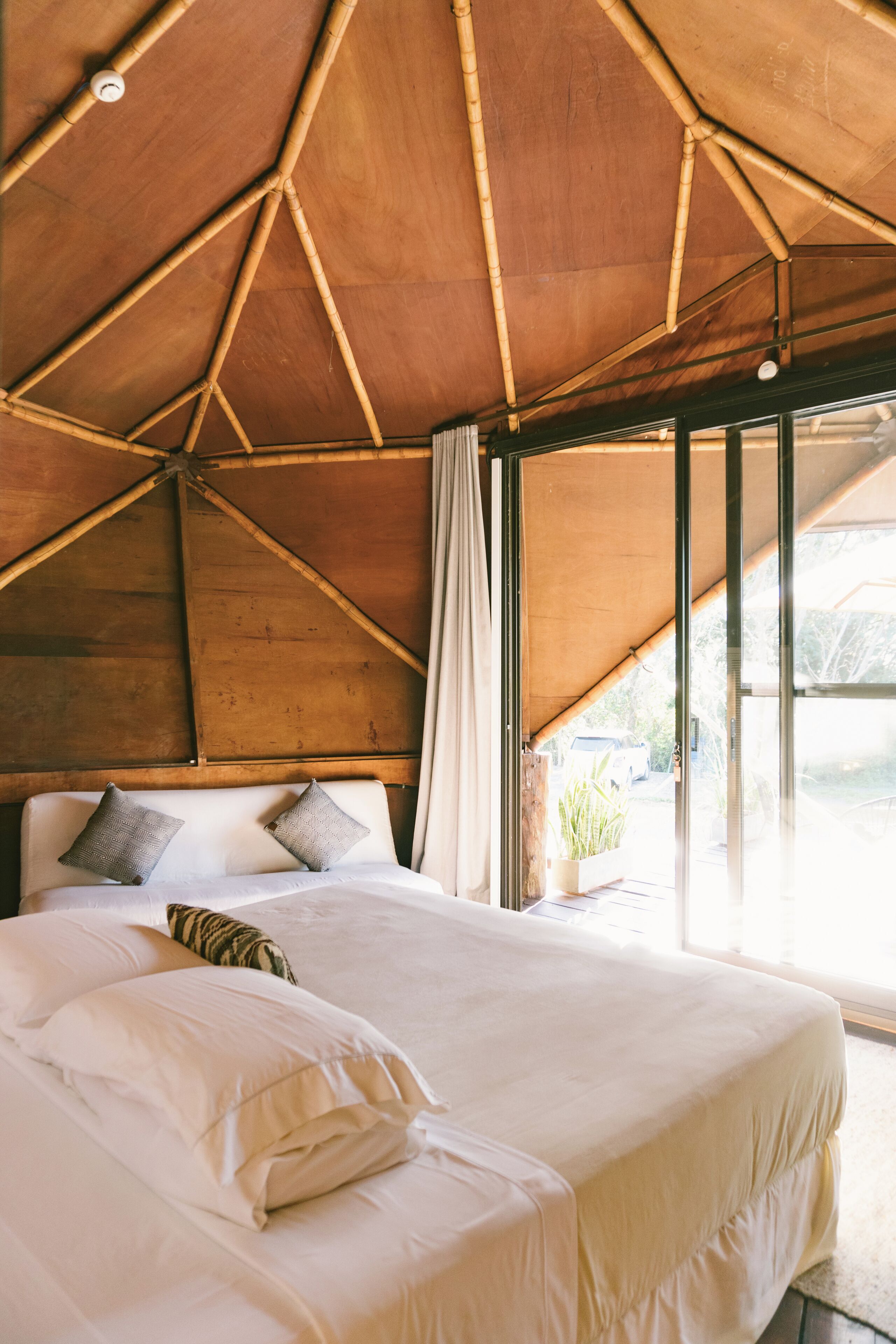Een kamer met een groot bed, houten balken in het plafond en een raam met gordijnen.