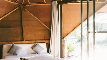Een kamer met een groot bed, houten balken in het plafond en een raam met gordijnen.