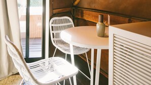 Canto de um quarto com uma mesa e cadeiras brancas, um abajur pendurado e uma janela com cortinas.