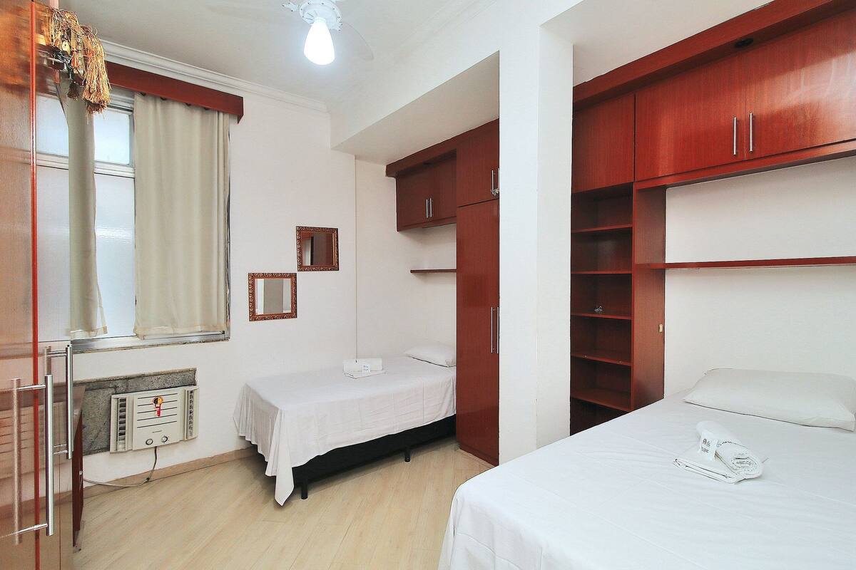 Une chambre à coucher comprenant un lit, une armoire, une table de chevet, un miroir et une fenêtre avec des rideaux.
