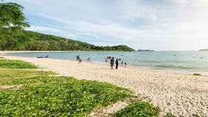 A beach with people walking and swimming, a boat on the water, and a forested hill in the background. - GetZleep House Sattahip (Sattahip)