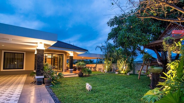 A modern house with a well-maintained garden, a paved walkway, and a small dog in the yard. - GetZleep House Sattahip (Sattahip)