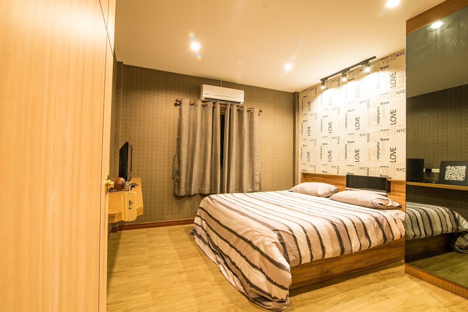 A bedroom with a bed, a TV, a bedside table, and a wall with 'NYC' and 'LOVE' printed on it.