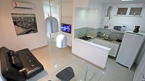 Una cuina moderna amb armaris blancs, un microones i una cafetera. A la zona d'estar hi ha un sofà de pell negra i dues cadires negres.