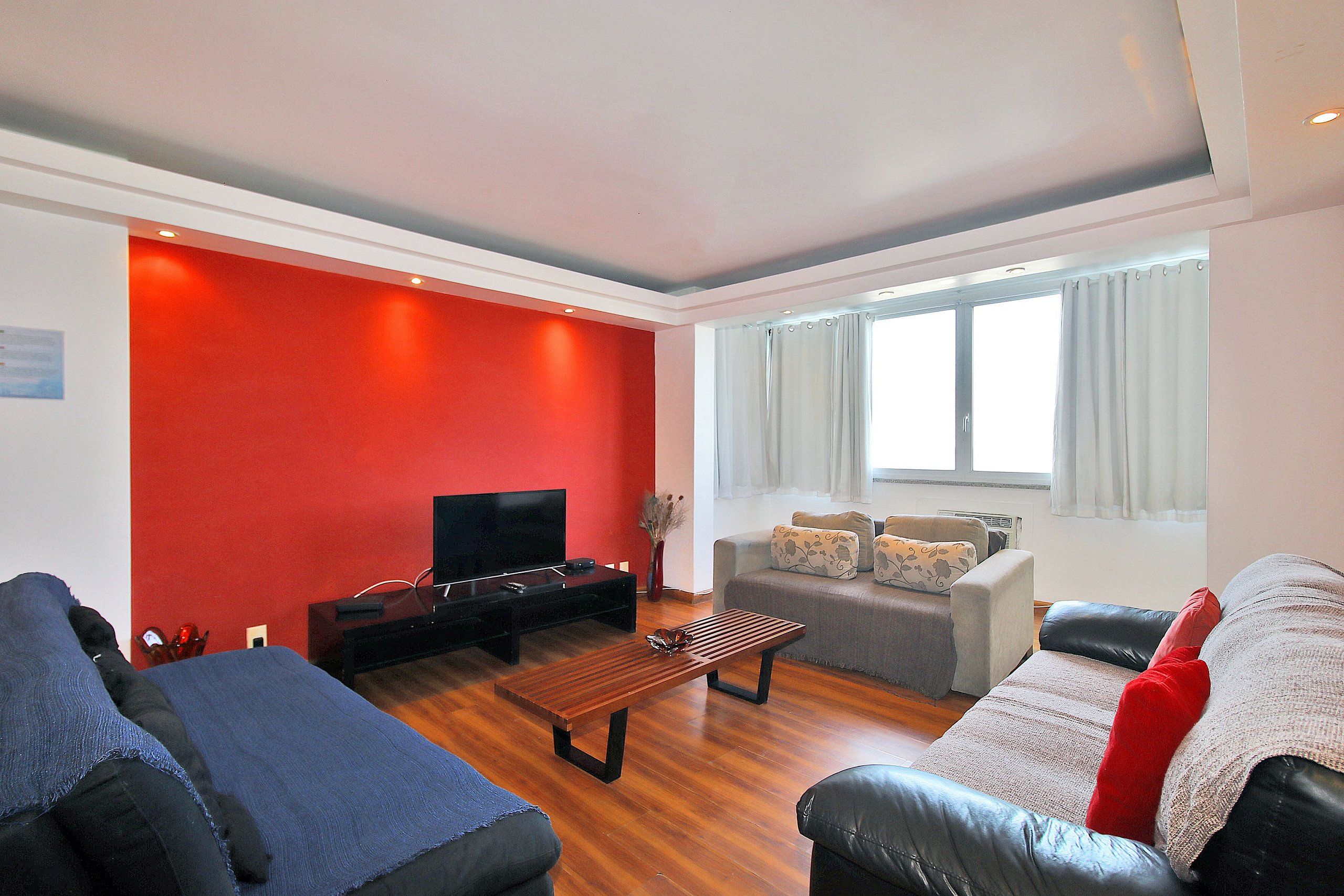 A living room with a red accent wall, a flat-screen TV, a wooden coffee table, and two sofas.