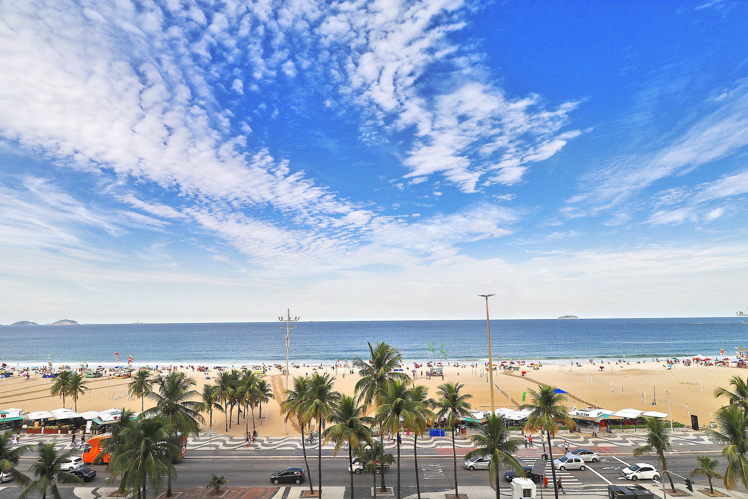 A beach with palm trees, a road, and a clear sky.