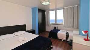 Hotelkamer met twee bedden, een bureau, een stoel, een bureaulamp en uitzicht op zee.