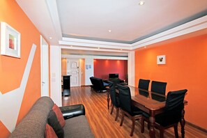 Uma sala de conferências com mesa de vidro e cadeiras pretas, paredes laranja e piso de madeira.