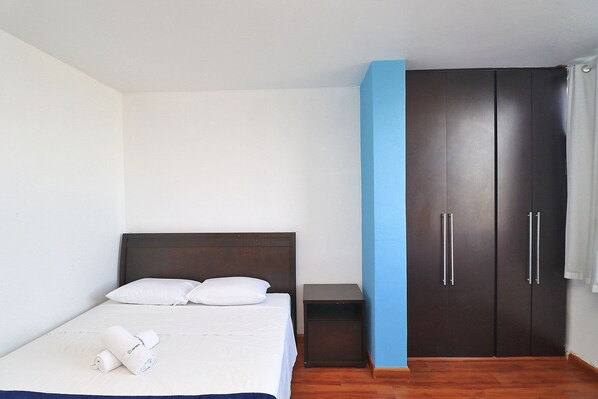 Quarto com cama, mesa de cabeceira e guarda-roupa.
