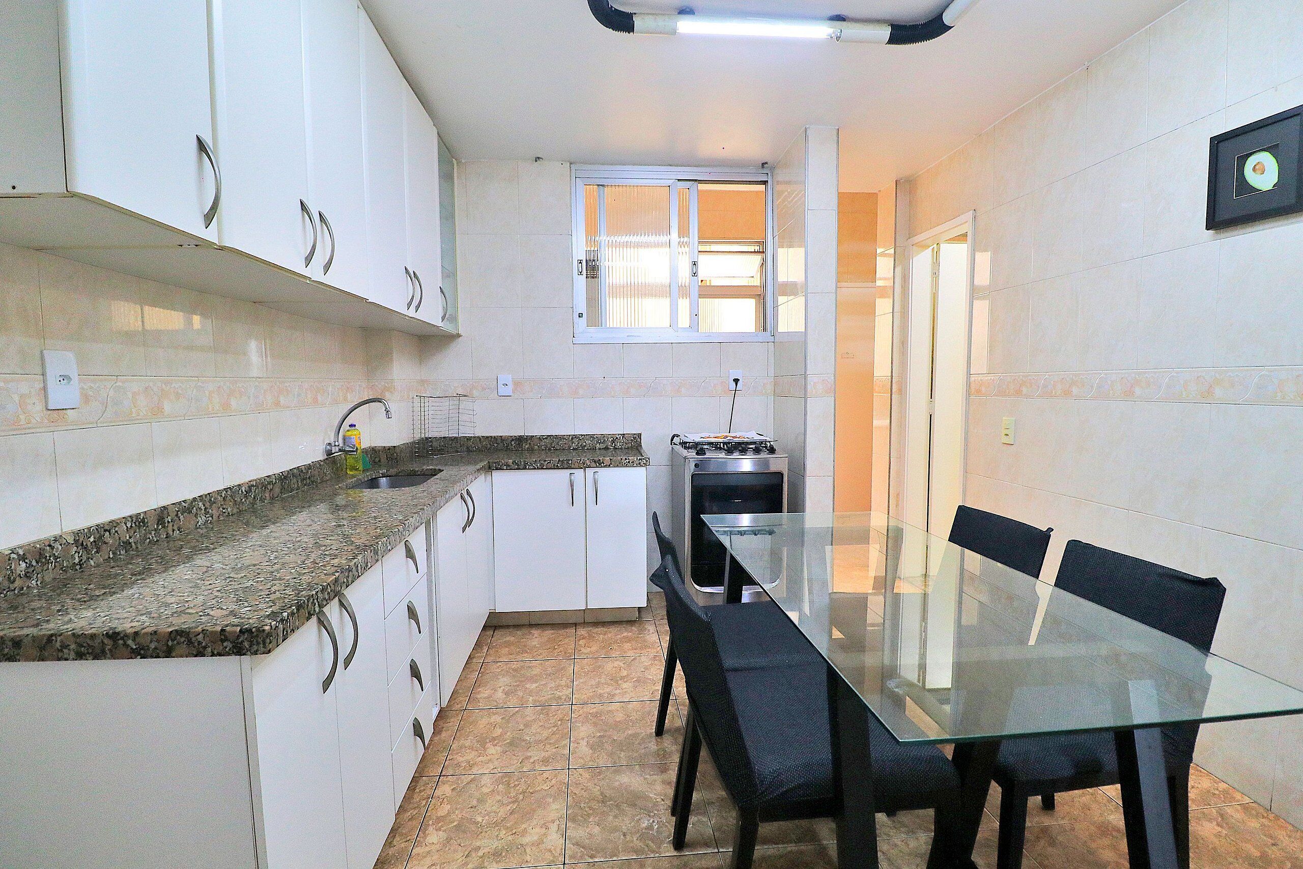 A compact kitchen with white cabinets, a granite countertop, a glass dining table, and black chairs.