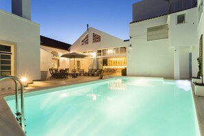 A swimming pool with lounge chairs and tables, a bar area, and a building with large windows. - Ericeira Soul (Mafra)