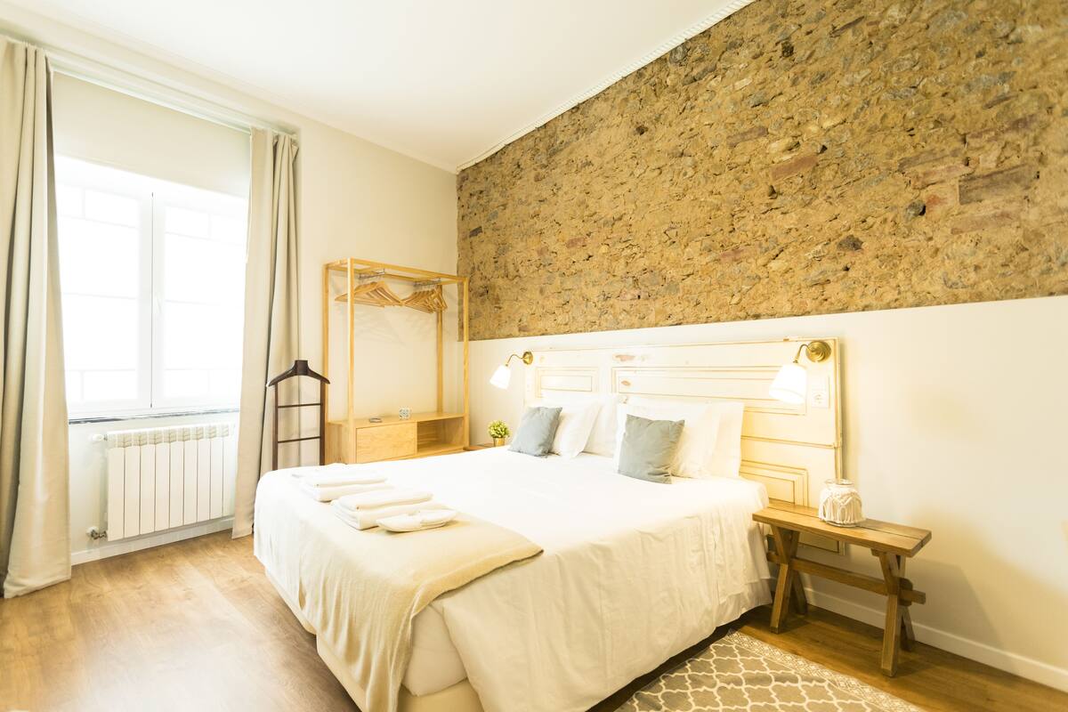 A bedroom with a large bed, a wooden bench, a nightstand, a mirror, and a radiator.