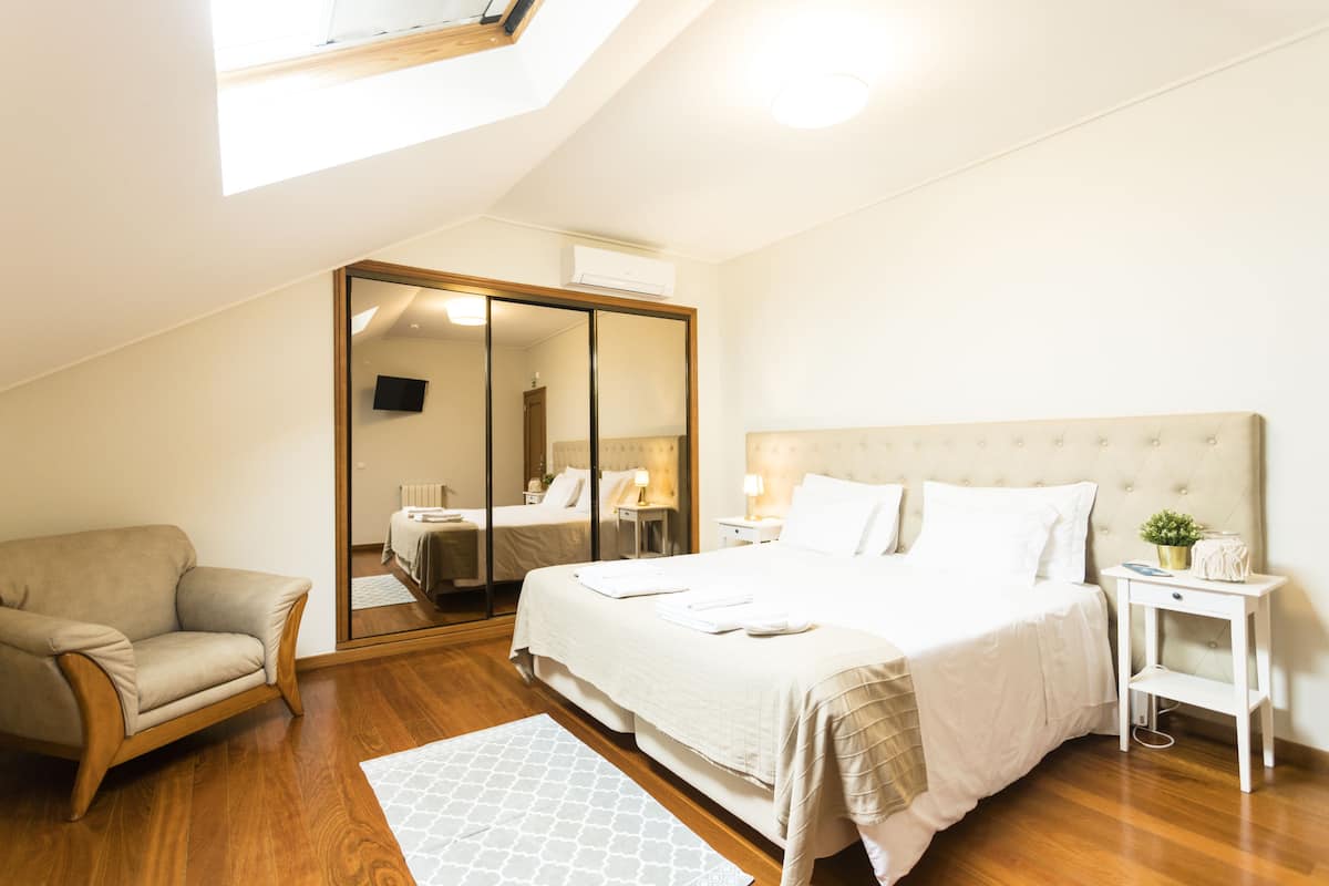 A bedroom with a large bed, a sofa, a mirror, and a skylight.