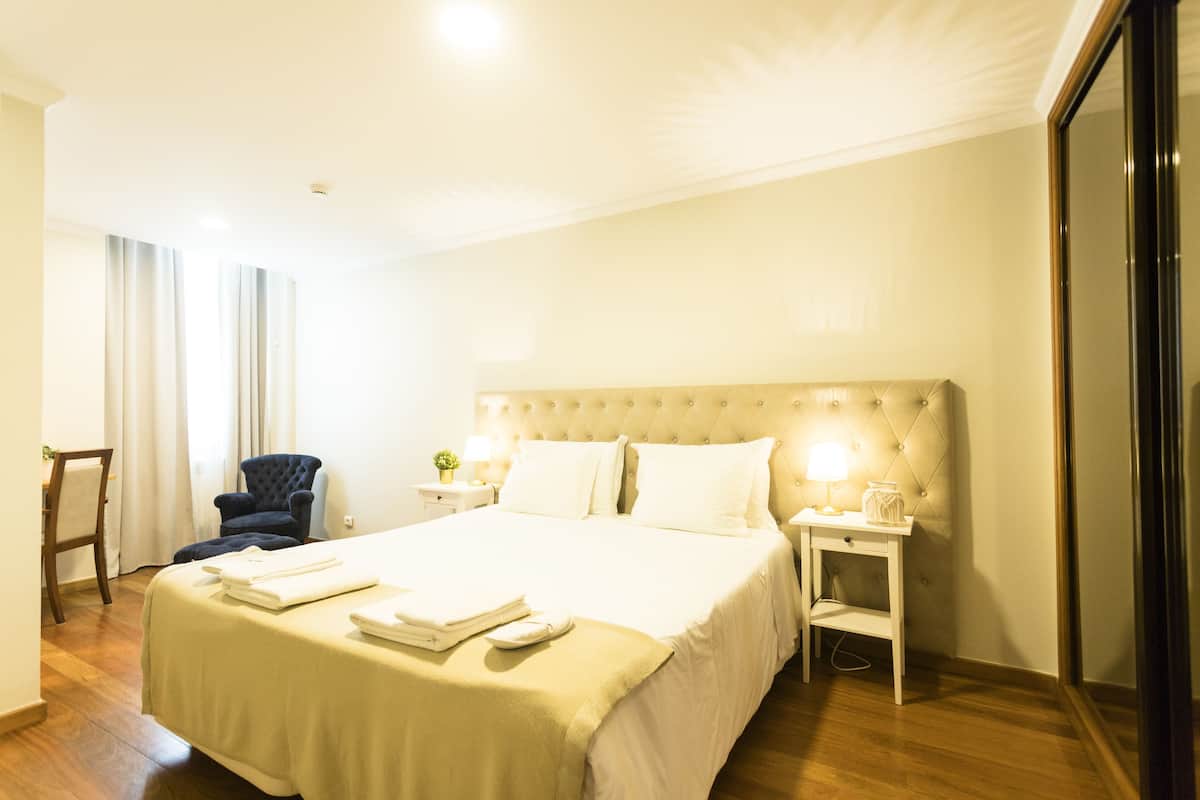 A hotel room with a large bed, a chair, a nightstand, and a mirror.