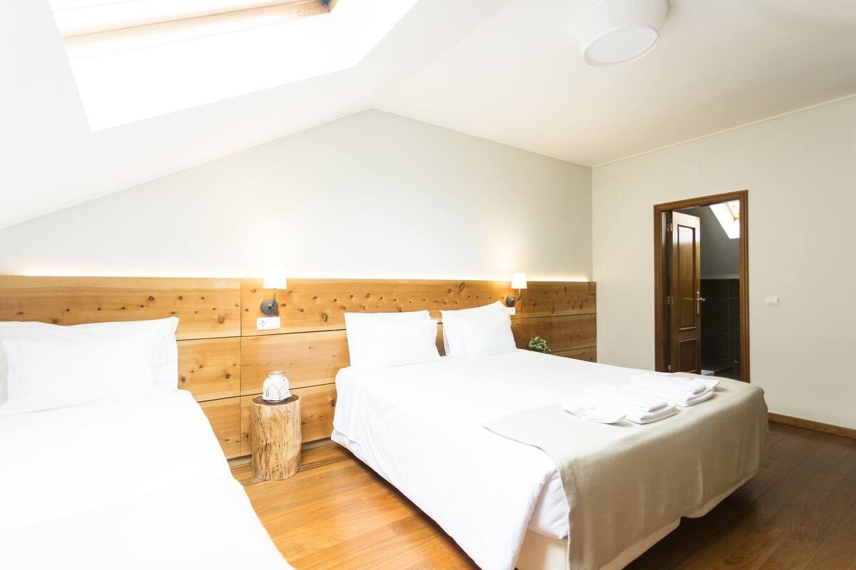 A bedroom with two beds, wooden headboard, skylight, and a wooden floor.
