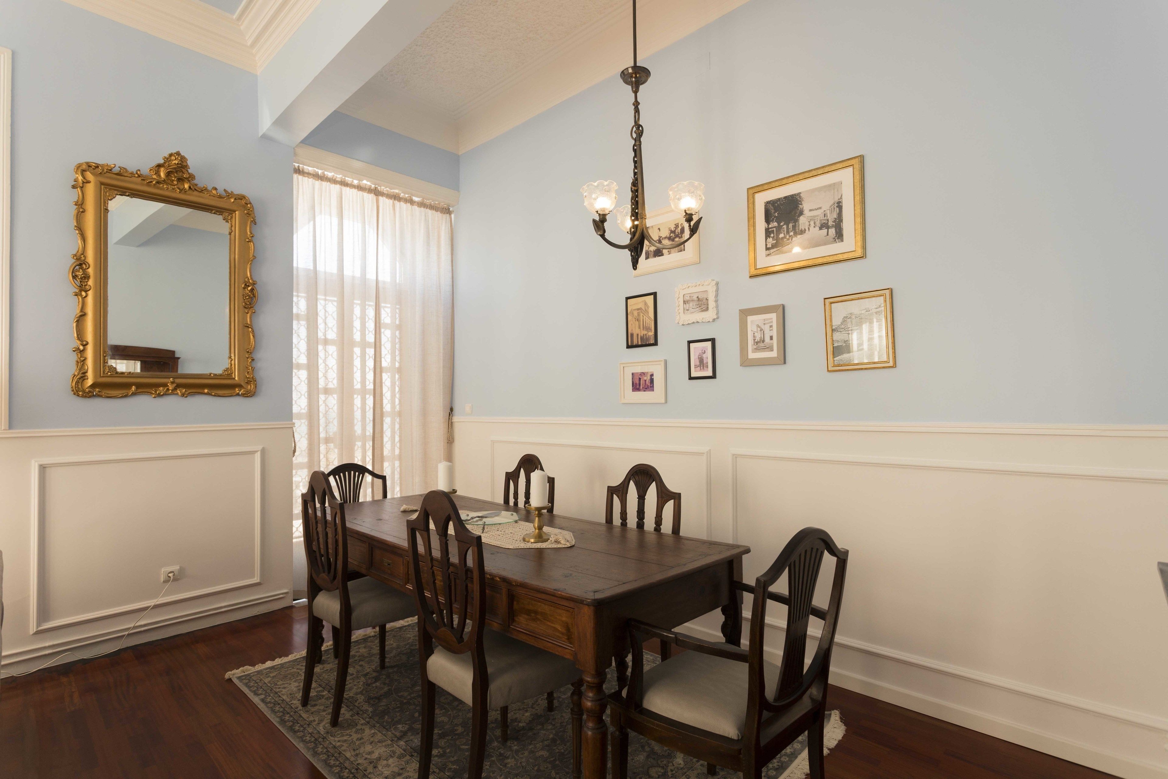 A dining room with a wooden table and chairs, a chandelier, and framed pictures on the wall.