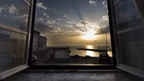 A view through a window of a building overlooking a body of water with a sunset. - Ericeira Soul (Mafra)