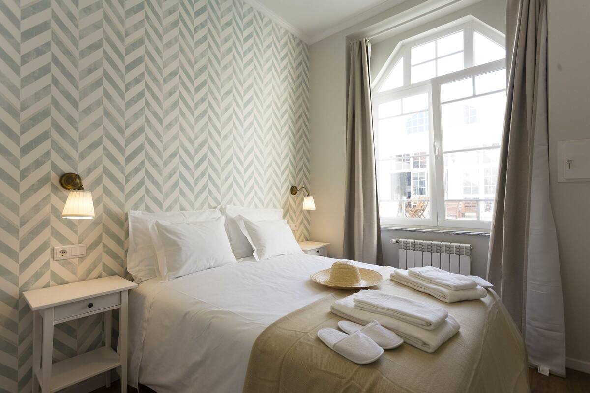 A neatly made bed with pillows, a bedside lamp, and a hat on the bed.