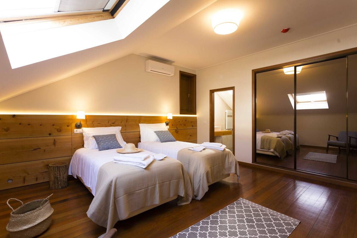 A bedroom with two beds, wooden headboard, skylight, and a large mirror.