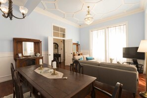 A dining area with a wooden table, chairs, and a chandelier. There is a living room with a sofa and a television. - Ericeira Soul (Mafra)
