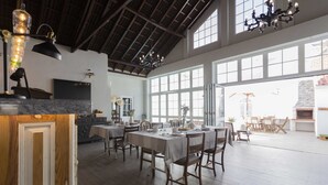 A spacious dining area with high ceilings and large windows, featuring a modern chandelier and a fireplace in the background. - Ericeira Soul (Mafra)