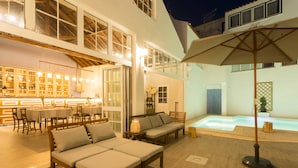 An outdoor seating area with a pool, wooden furniture, and a bar with illuminated shelves. - Ericeira Soul (Mafra)