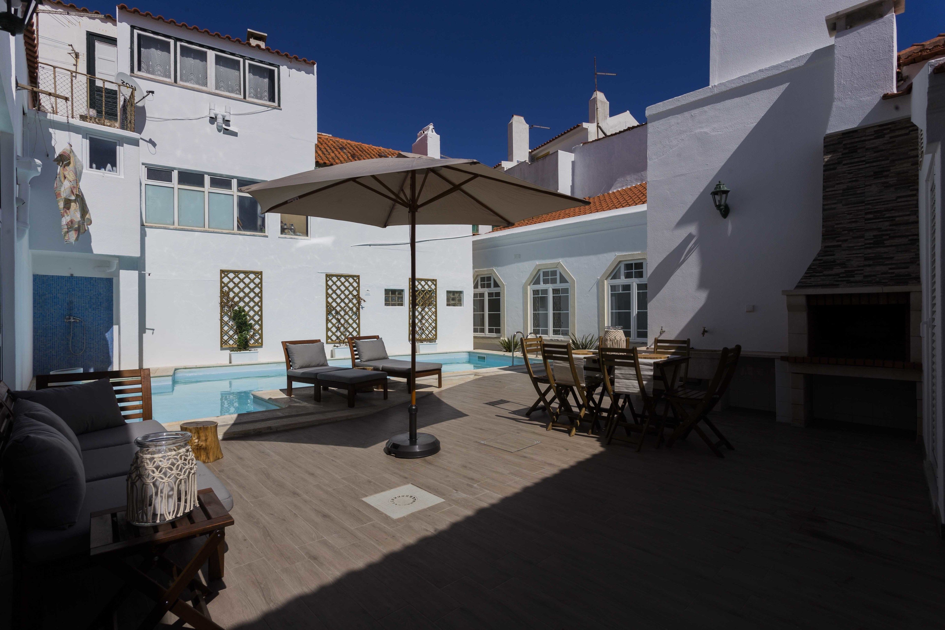 A poolside area with a sun lounger, a table with chairs, and a large umbrella.