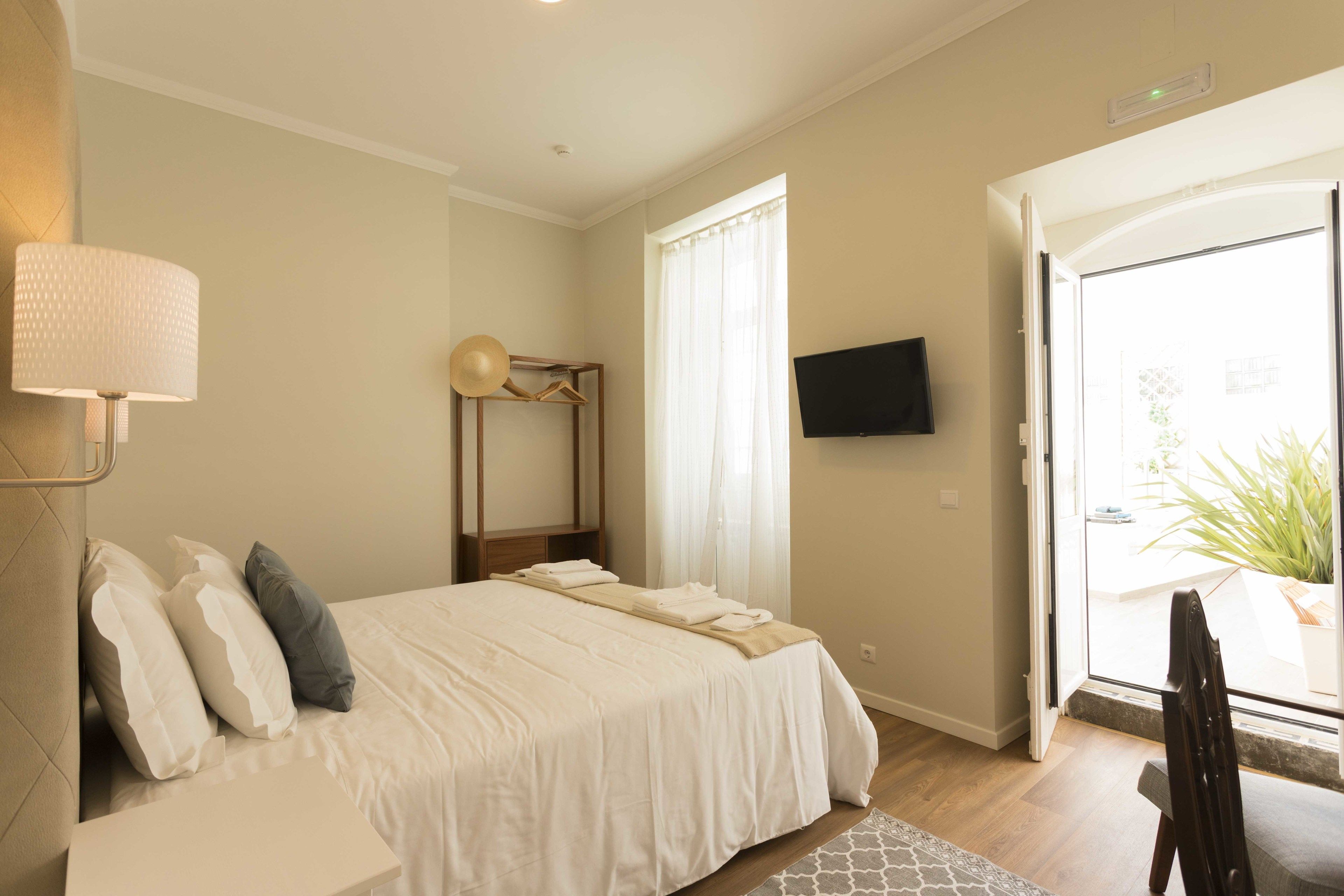 A bedroom with a bed, pillows, a bedside lamp, a TV, and a window with curtains.