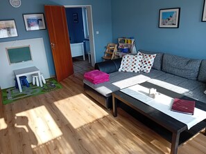 Ein Wohnzimmer mit einer Couch, einem Couchtisch, einem kleinen Tisch mit Hocker, einem Bücherregal und einer Tür zu einem anderen Raum.