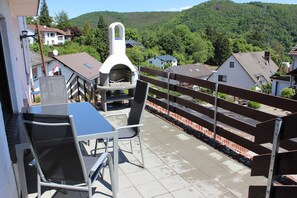 Eine Terrasse mit Grill, Sitzgelegenheit und Blick auf eine Hügellandschaft.