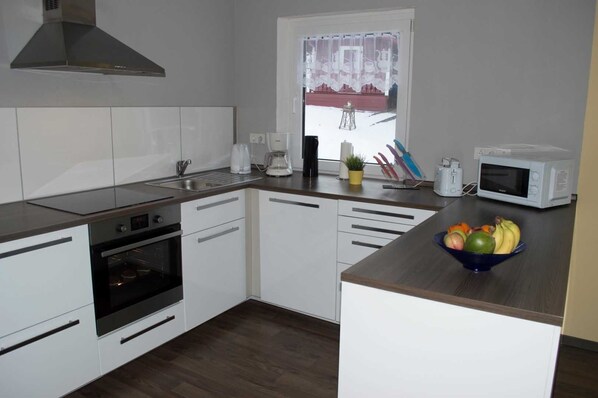A modern kitchen with white cabinets, a microwave, a coffee maker, and a fruit bowl on the counter.