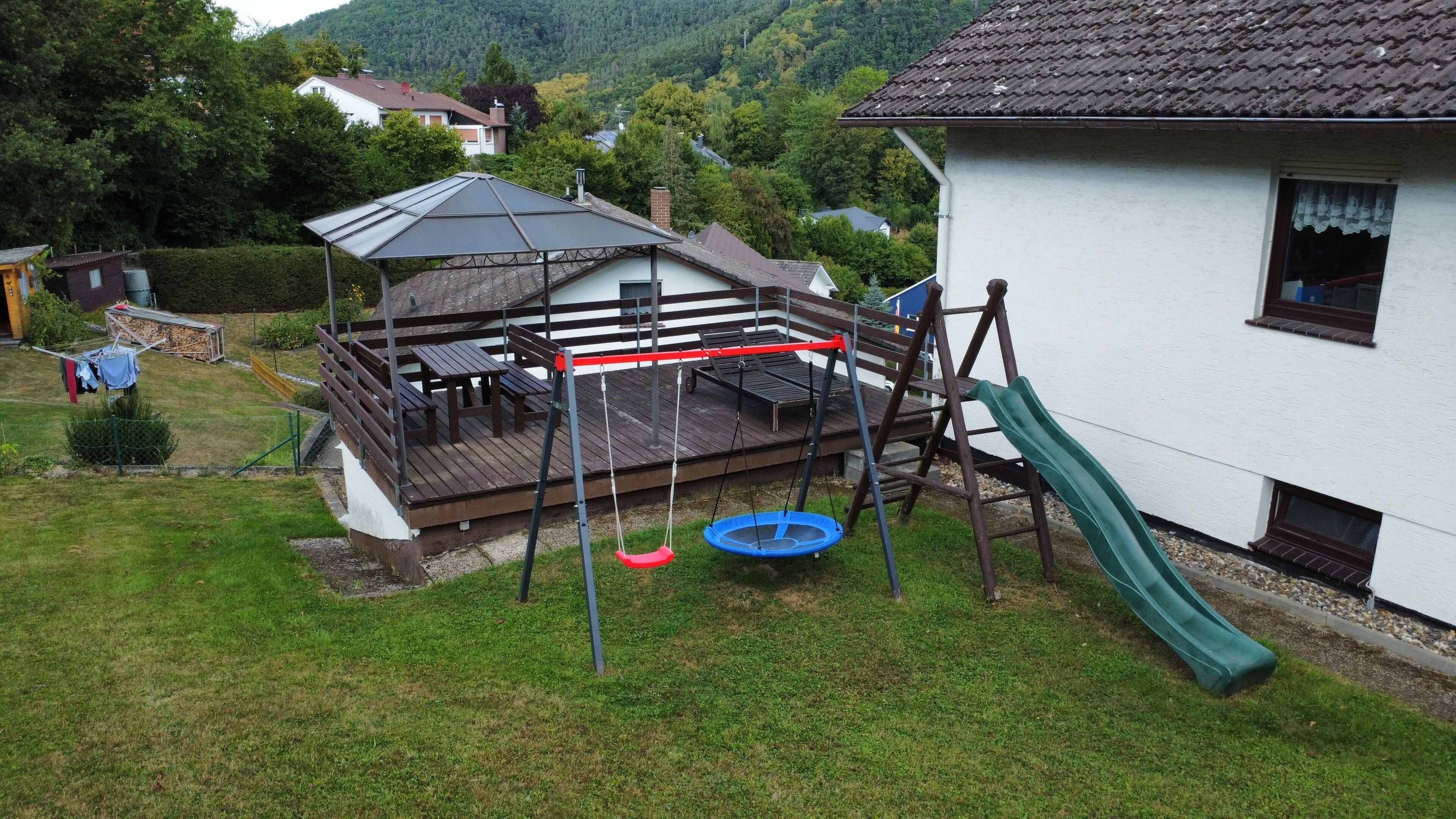 A residential area with a wooden deck, a swing set, and a slide.